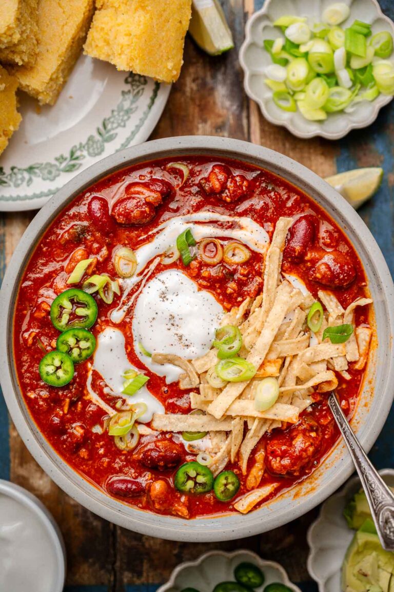 a bowl of vegan chili with kidney beans and vegetarian tvp beef topped with dairy-free sour cream, green onions and tortilla strips.
