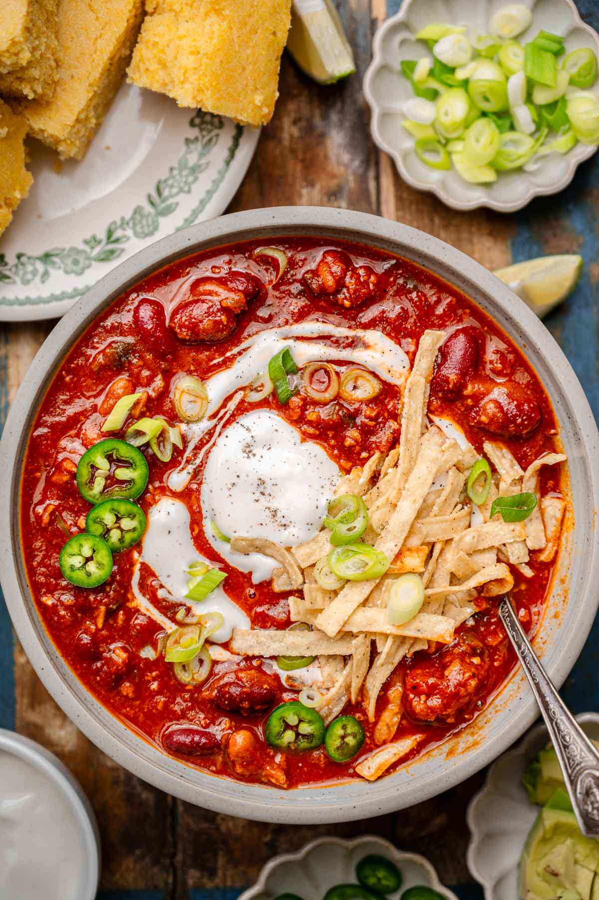 a bowl of vegan chili with kidney beans and vegetarian tvp beef topped with dairy-free sour cream, green onions and tortilla strips.
