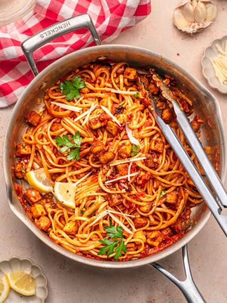Vegan linguine with paprika tofu and chili flakes in a stainless steel pan.