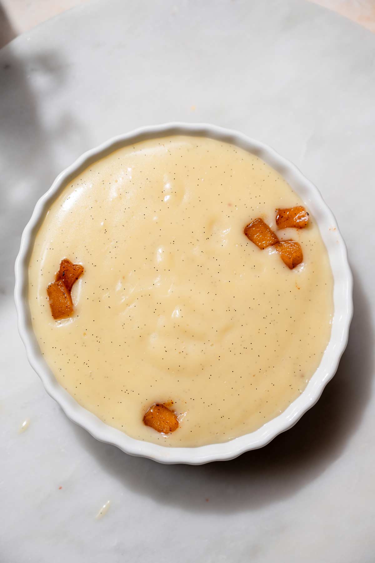 Smooth vanilla bean custard layered over spiced apple filling in a white ramekin, ready to chill.
