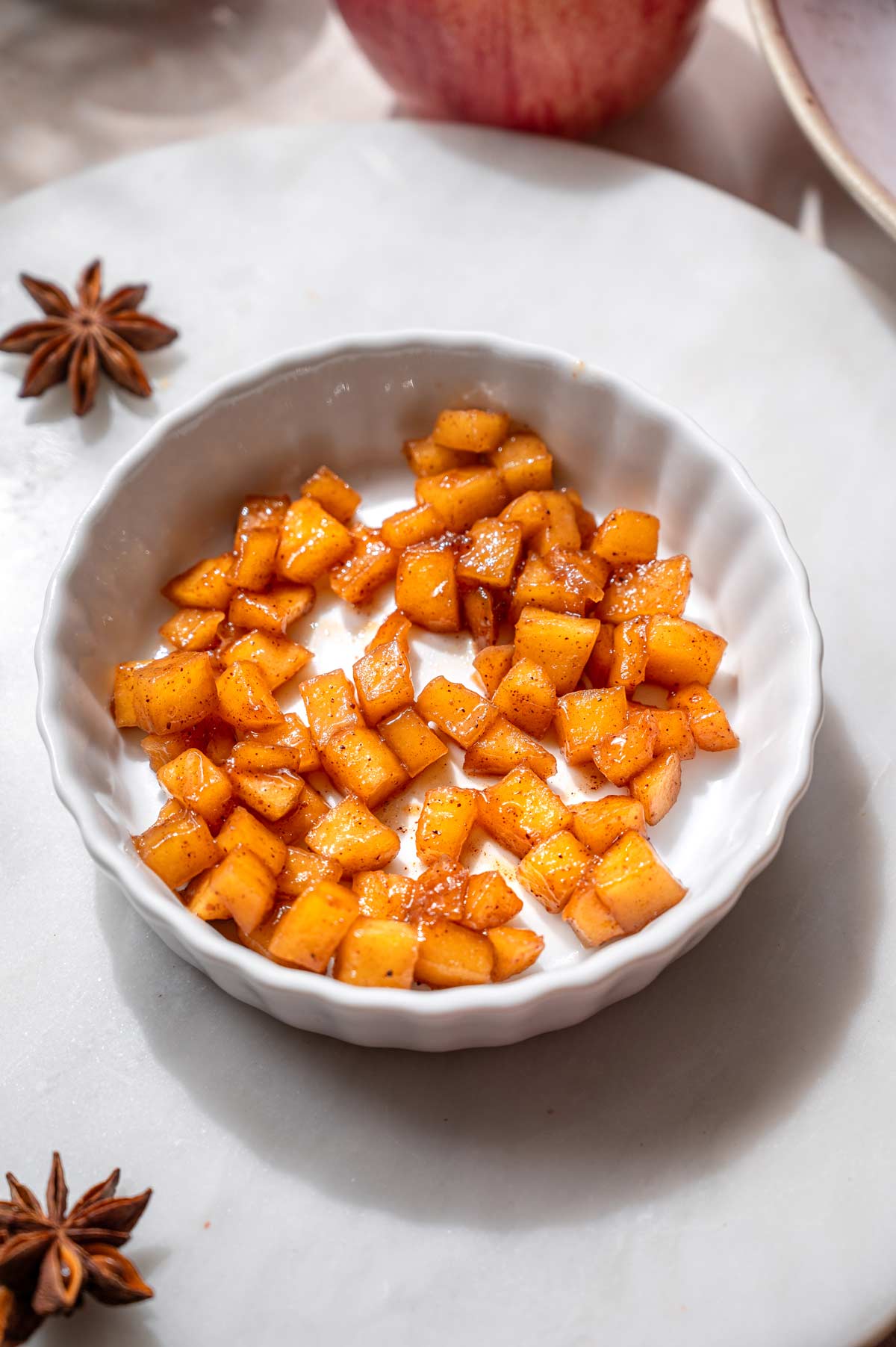 A layer of cooked cinnamon apples spooned into a white ceramic ramekin before adding the custard.