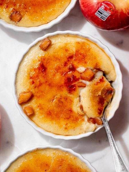 Overhead view of apple pie crème brûlée with a spoonful of creamy vanilla custard, cinnamon apples, and cracked caramelized sugar.