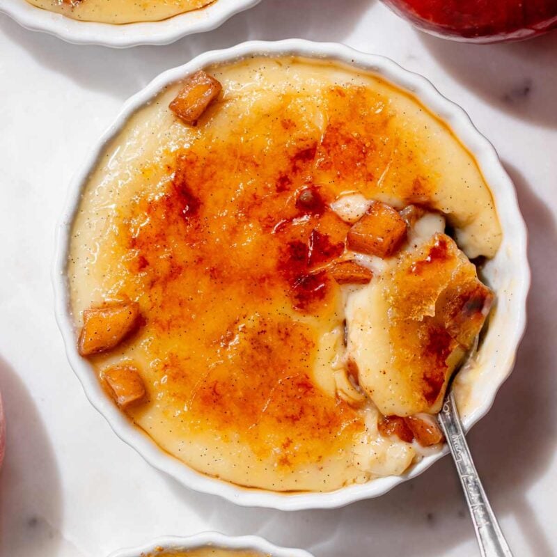 Overhead view of apple pie crème brûlée with a spoonful of creamy vanilla custard, cinnamon apples, and cracked caramelized sugar.