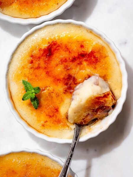 Overhead view of vegan crème brûlée with a golden caramelized sugar crust and a spoonful of creamy vanilla bean custard.