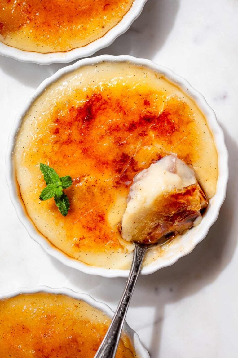 Overhead view of vegan crème brûlée with a golden caramelized sugar crust and a spoonful of creamy vanilla bean custard.