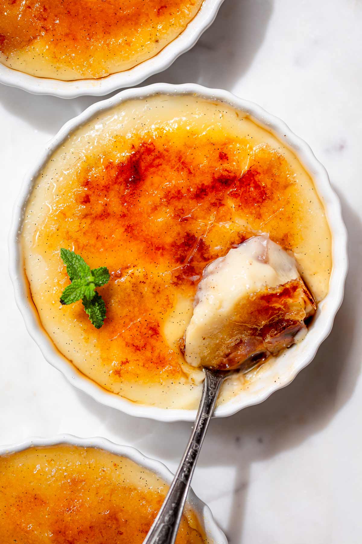 Overhead view of vegan crème brûlée with a golden caramelized sugar crust and a spoonful of creamy vanilla bean custard.