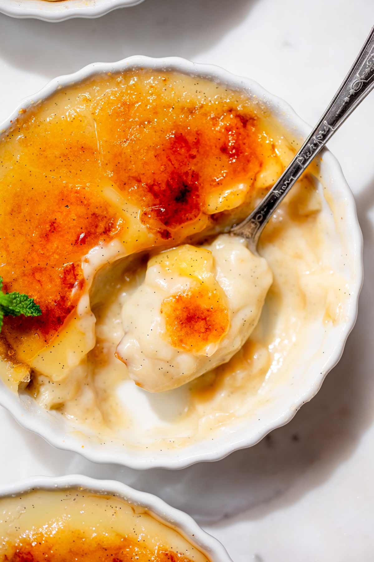 Spoon lifting a scoop of creamy dairy-free vanilla custard through the golden, cracked sugar topping of crème brûlée.