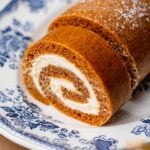 Close-up of a soft pumpkin sponge rolled around a thick cream cheese filling on a blue floral platter.