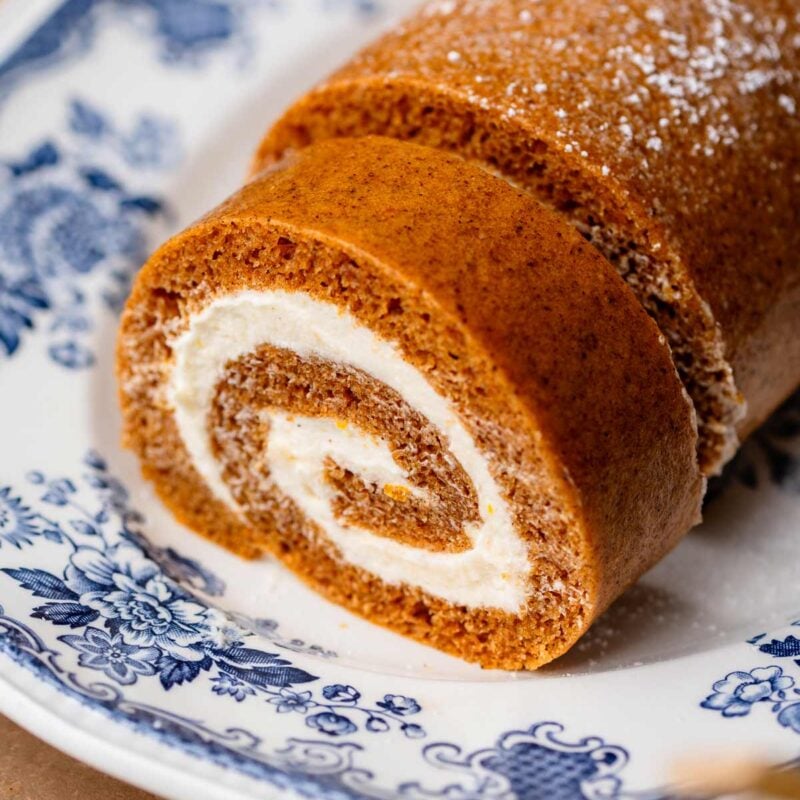 Close-up of a soft pumpkin sponge rolled around a thick cream cheese filling on a blue floral platter.