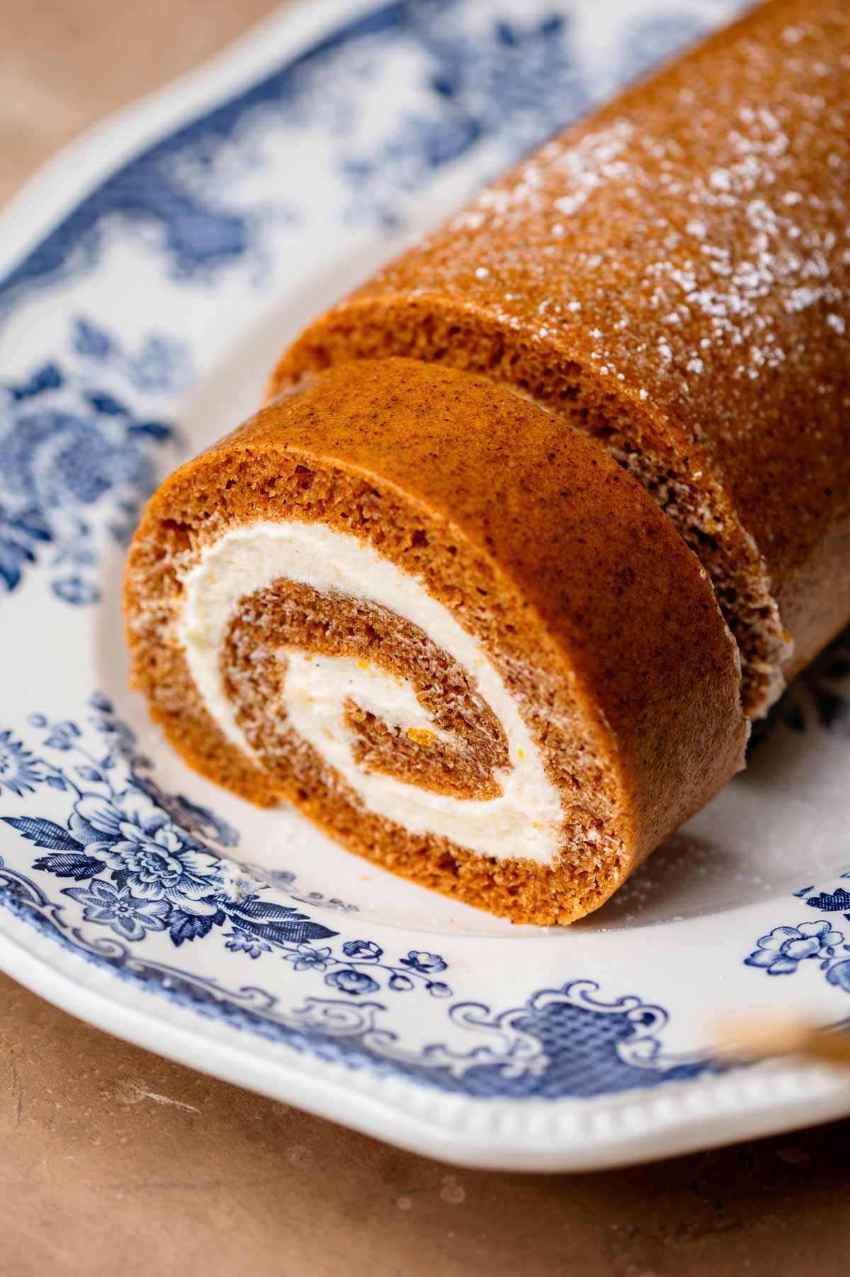 Close-up of a soft pumpkin sponge rolled around a thick cream cheese filling on a blue floral platter.