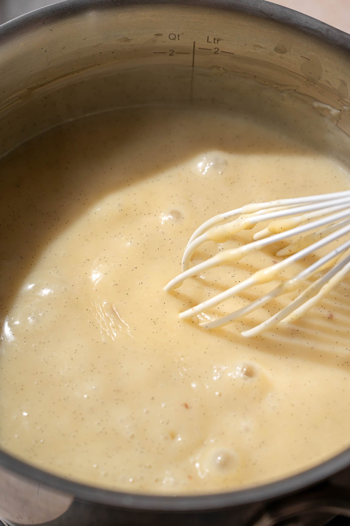 Thickened vanilla custard bubbling gently in a saucepan with a whisk.