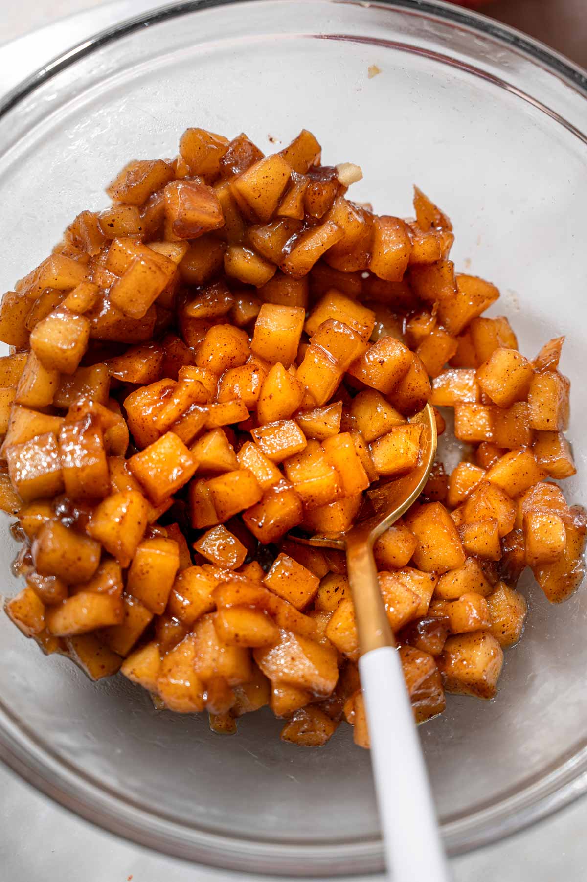 Tender diced apples coated in a glossy, cinnamon-spiced apple pie filling in a glass bowl.
