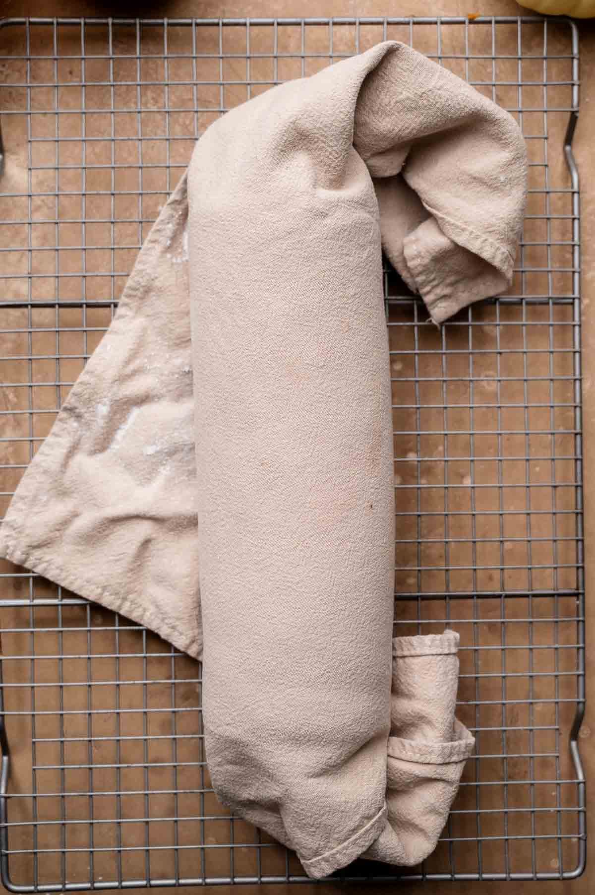 Pumpkin sponge cake rolled inside a kitchen towel and resting on a wire cooling rack.