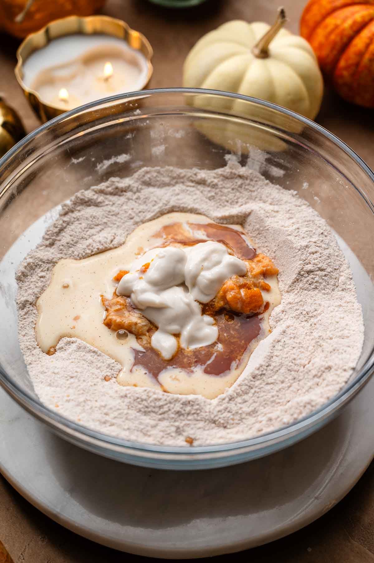 Pumpkin puree, dairy-free yogurt, and other wet ingredients added to a bowl of dry cake ingredients.