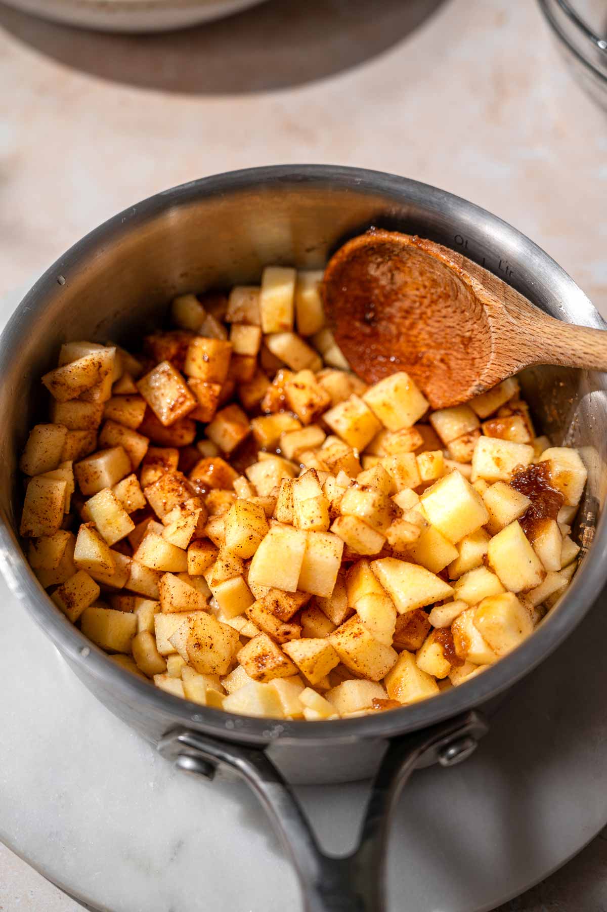 Small diced apples tossed with cinnamon and spices in a saucepan with a wooden spoon.