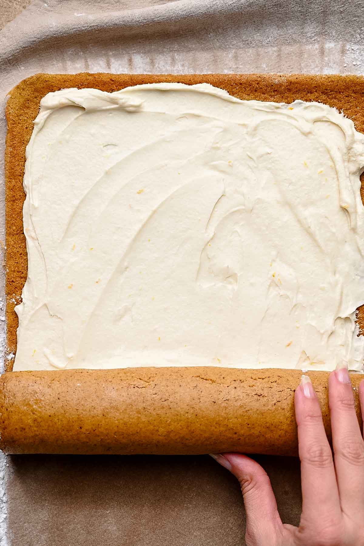 Pumpkin sponge spread with cream cheese frosting being carefully rolled into a spiral.
