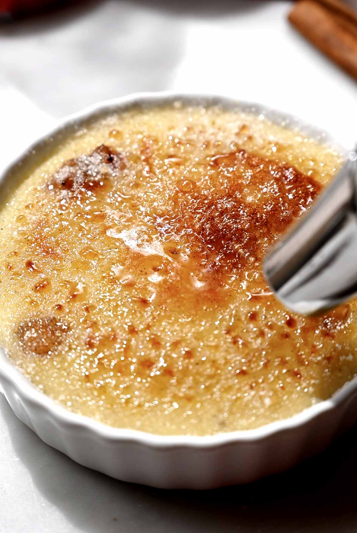 A kitchen torch melting and browning a thin layer of sugar over custard in a white ramekin.