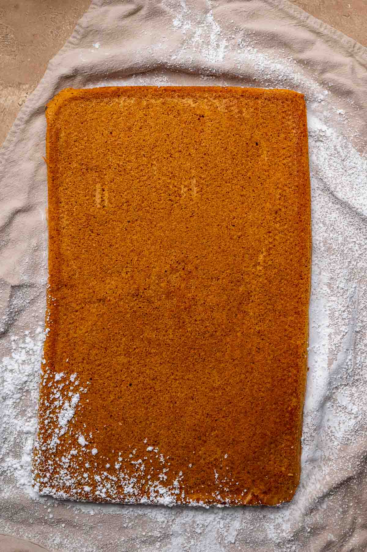 Finished pumpkin jelly roll lightly dusted with powdered sugar on a linen towel.