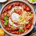 a bowl of vegan chili with kidney beans and vegetarian tvp beef topped with dairy-free sour cream, green onions and tortilla strips.