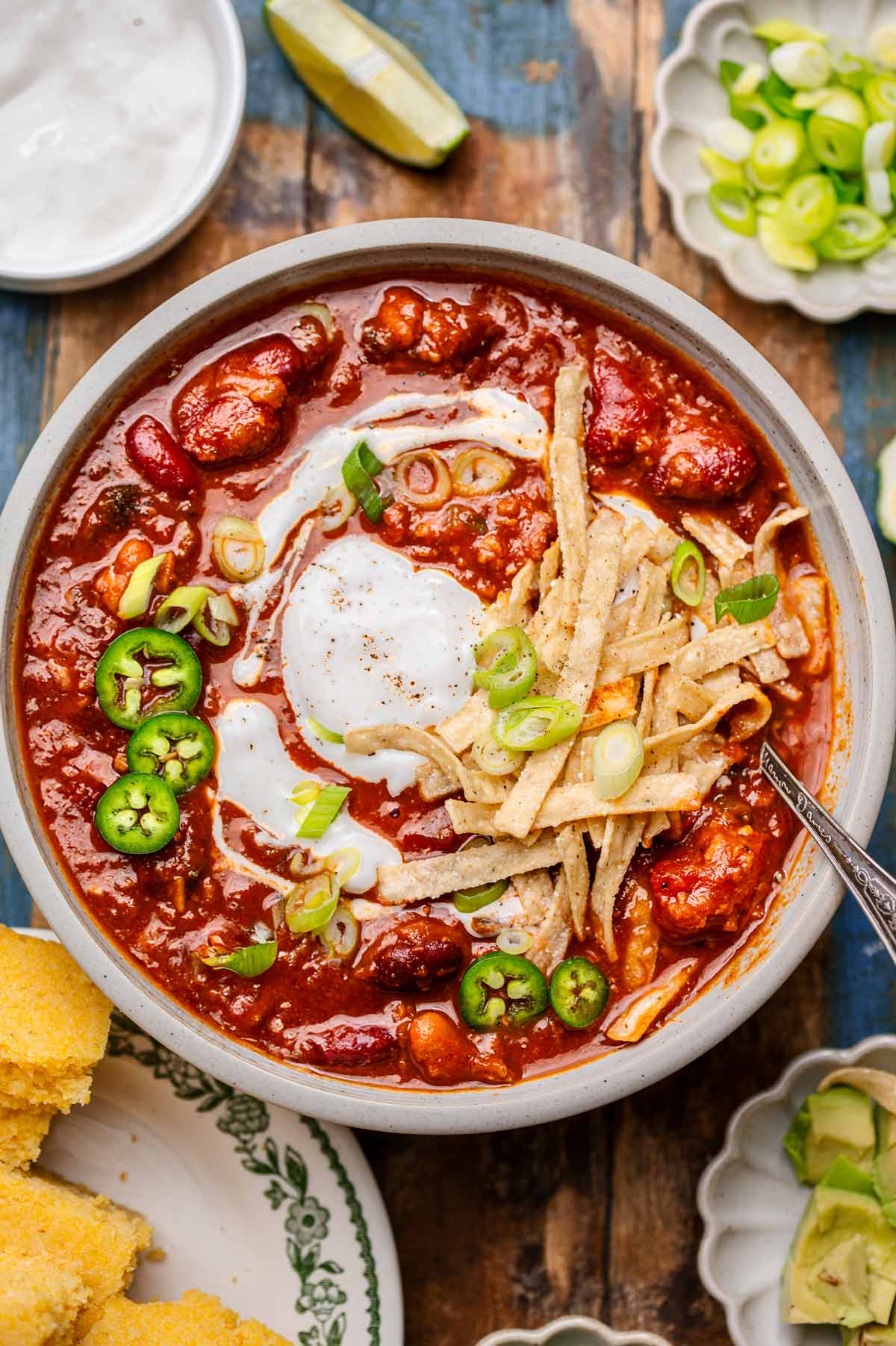 a bowl of vegan chili with kidney beans and vegetarian tvp beef topped with dairy-free sour cream, green onions and tortilla strips.