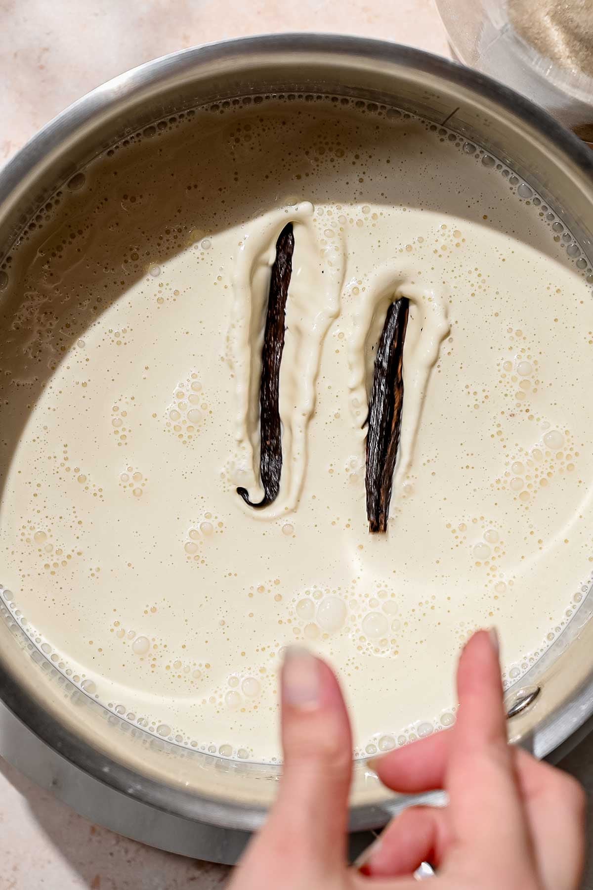 Split vanilla bean pods steeping in a saucepan of warm dairy-free milk.