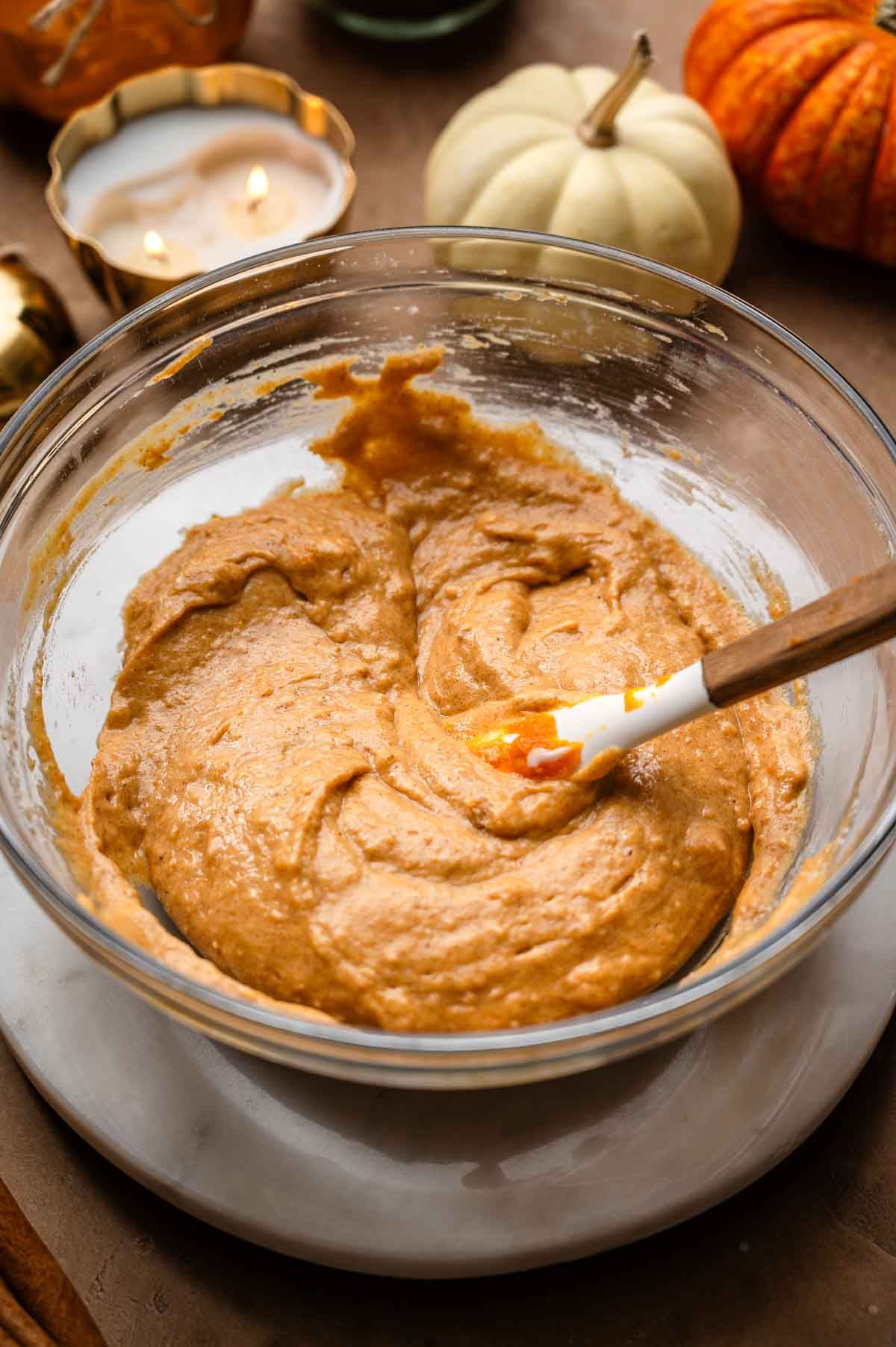 Thick orange pumpkin cake batter in a glass mixing bowl with a spatula.
