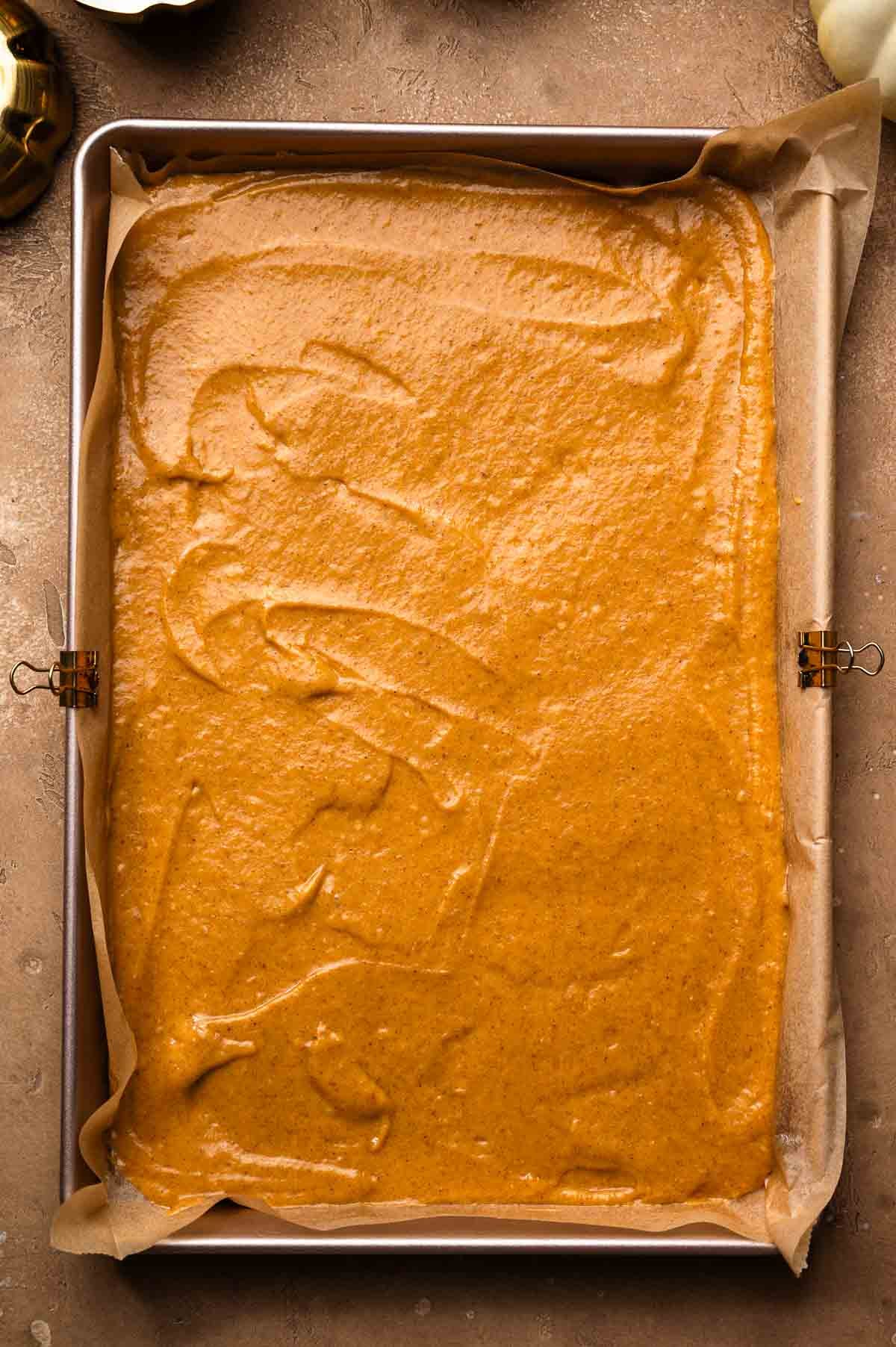 Smooth pumpkin spice cake batter spread evenly in a parchment-lined baking pan.