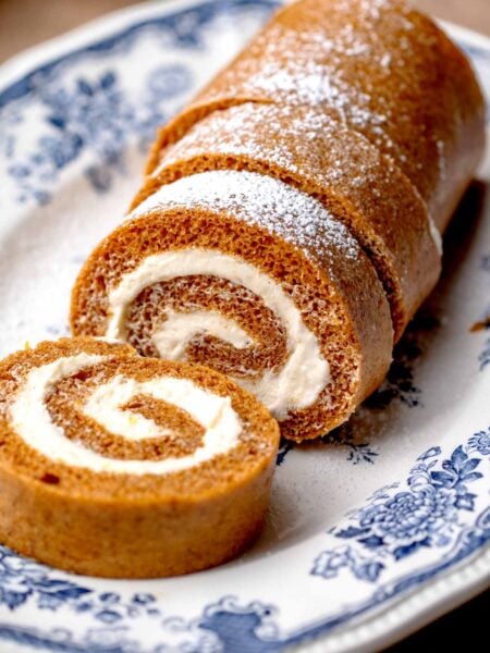 Pumpkin roll cake dusted with powdered sugar, with a slice cut to reveal the cream cheese filling.