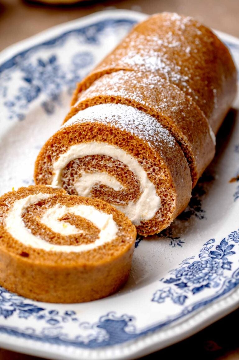 Pumpkin roll cake dusted with powdered sugar, with a slice cut to reveal the cream cheese filling.