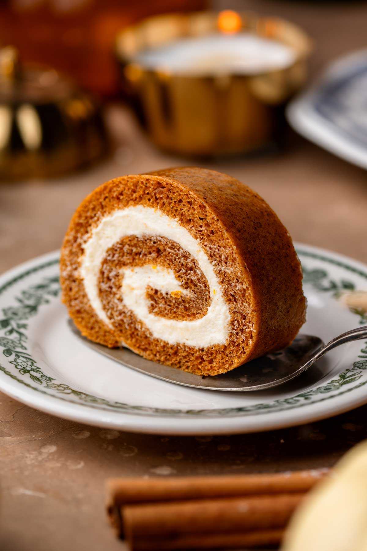 Single slice of pumpkin roll on a silver serving spatula, showing the spiral of cake and creamy filling.