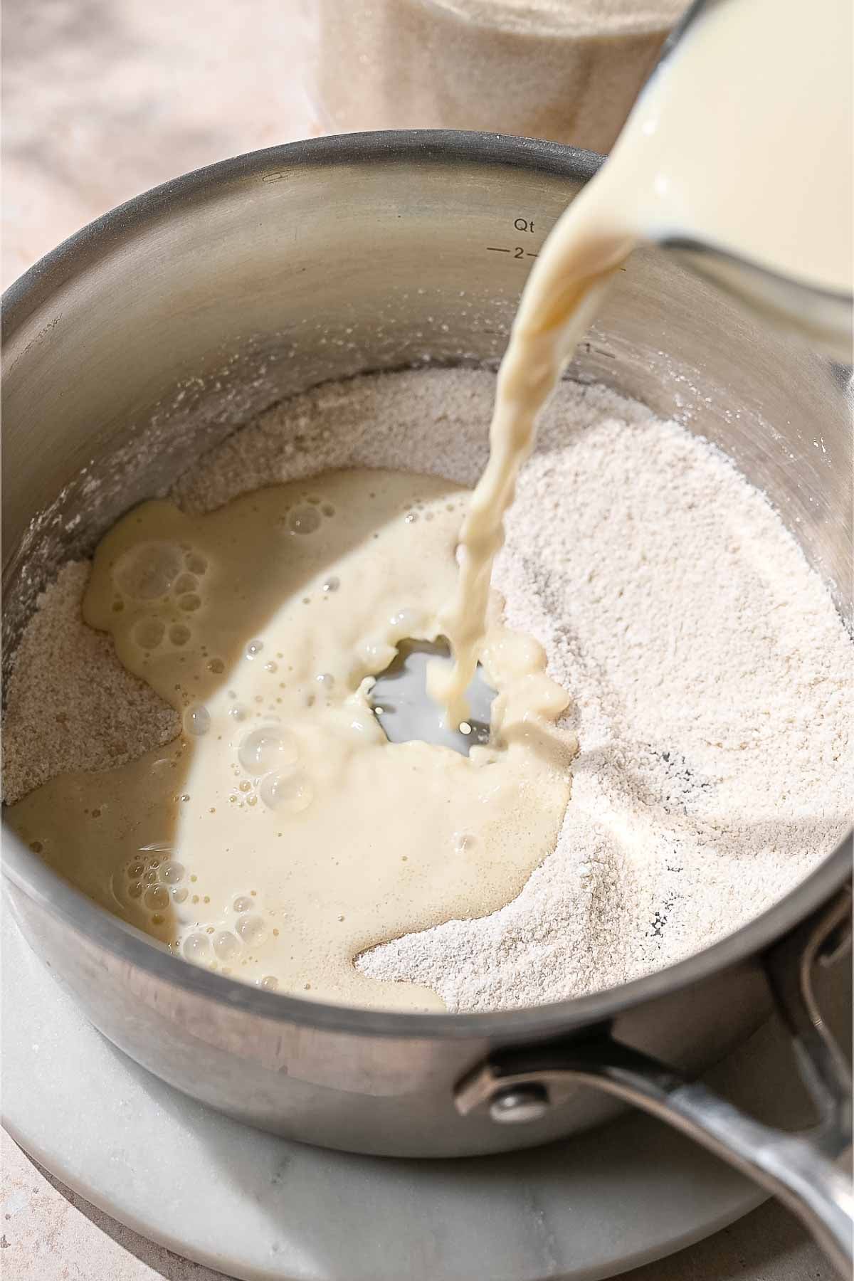 Soy milk being added to a saucepan containing sugar and cornstarch to make an eggless custard.