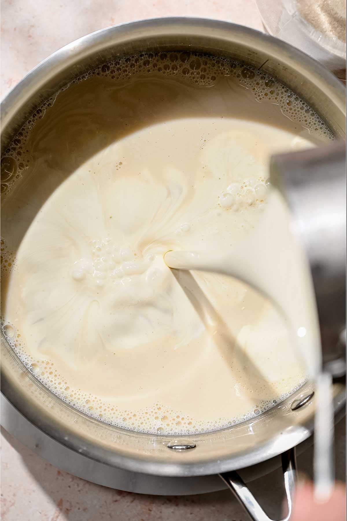Plant-based heavy cream being poured into a saucepan of soy milk.